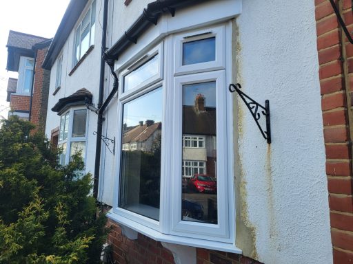 Bay window installation A bay window with white frames and brackets, set against a brick wall.