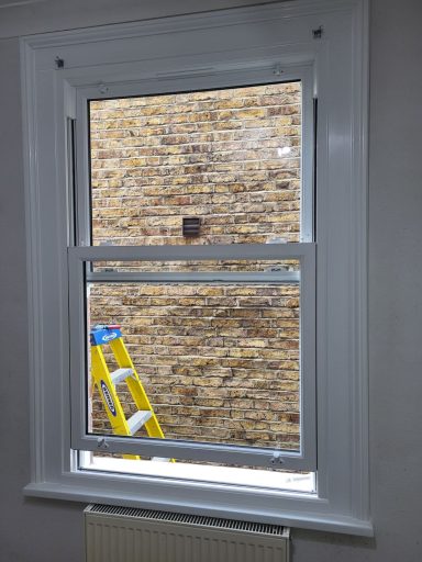 UPVC Sash Window Window frame with a view of a brick wall and a yellow ladder outside.
