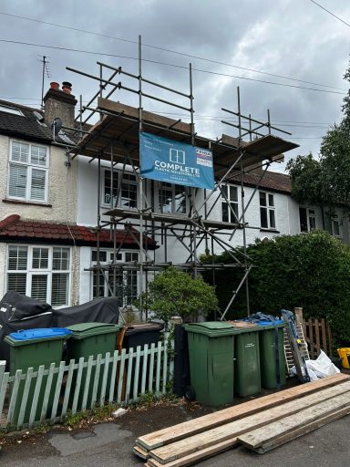 Scaffolding in front of a house with bins and construction materials nearby.