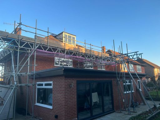 Scaffolded residential building under construction against a clear blue sky.