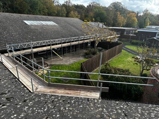 Construction scaffolding around a building with gardens and trees in the background.