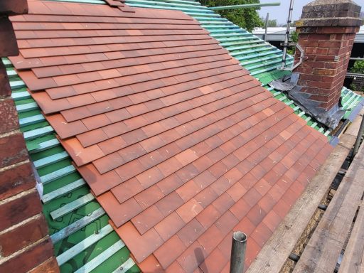 Roofing Surrey Newly laid red roof tiles on a sloped roof with green underlay and chimney.