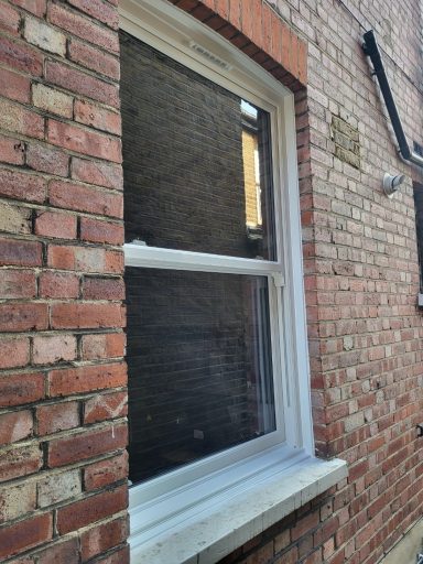 UPVC Vertical Sliding Window A closed window with a darkened pane set in a brick wall.