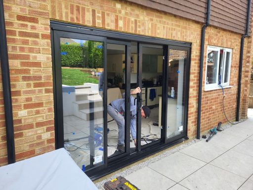 Aluminium Door Installation. A person installing glass doors in a brick house with a garden view.