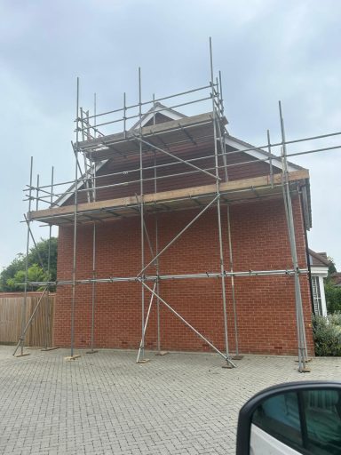 Red brick house partially covered in scaffolding for construction work.