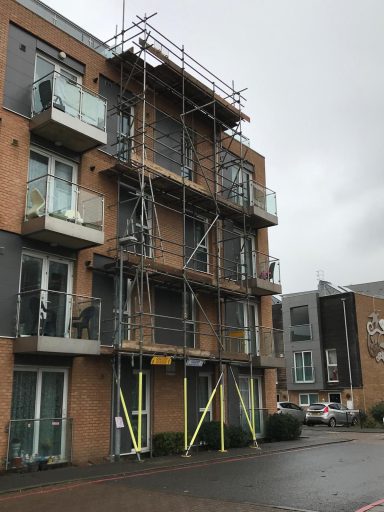 Scaffolding surrounds a modern brick building under construction on a cloudy day.
