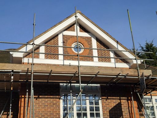 Fascia, Soffit and Guttering Replacement Construction scaffolding around a brick house with a circular window on the gable.