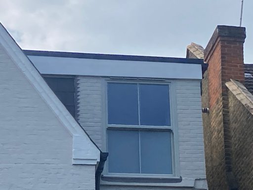 Flat Roofing And Sash Window White house with a large, modern window under a cloudy sky.