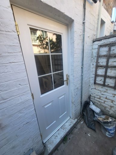 Rockdoor Installation, Richmond. White door with window panels, located next to a brick wall and debris.