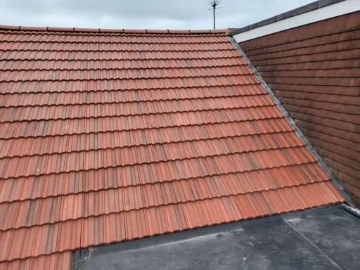 Roof Replacement Thames Ditton Red tiled roof with a sloped surface and a brick wall in the background.